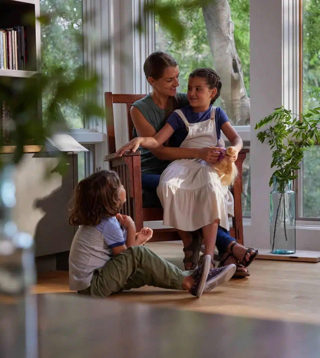 A Mother Sits With Her Two Children In A Bright, Cozy Room.