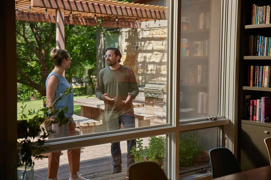 Aptive Pest Control Specialist Speaks With A Homeowner Outside On A Patio, Viewed Through A Window.