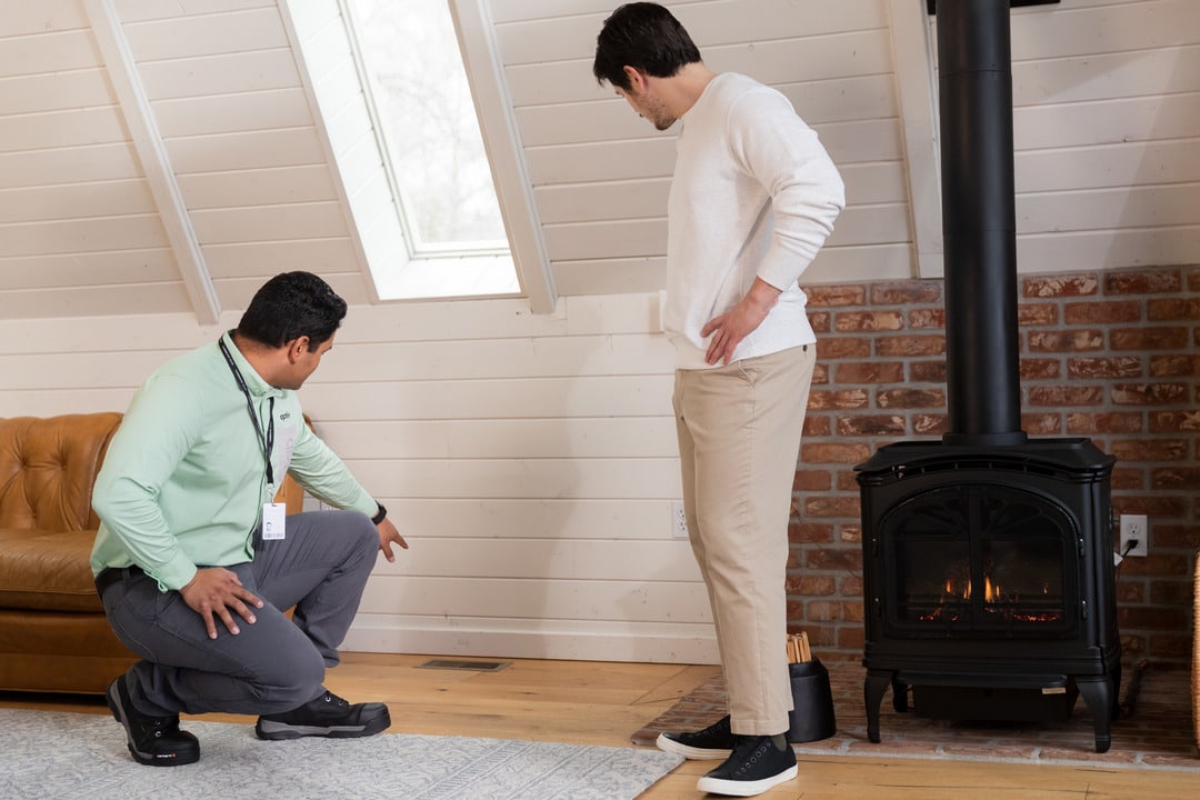 t: Aptive pest control specialist inspecting a floor vent with a homeowner in a cozy attic space.