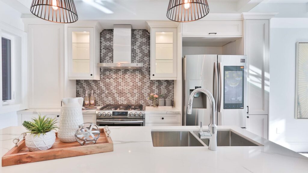 Modern Kitchen With White Cabinets, Stainless Steel Appliances, And A Decorative Tile Backsplash, Featuring A Wooden Tray With Decorative Items On The Countertop.