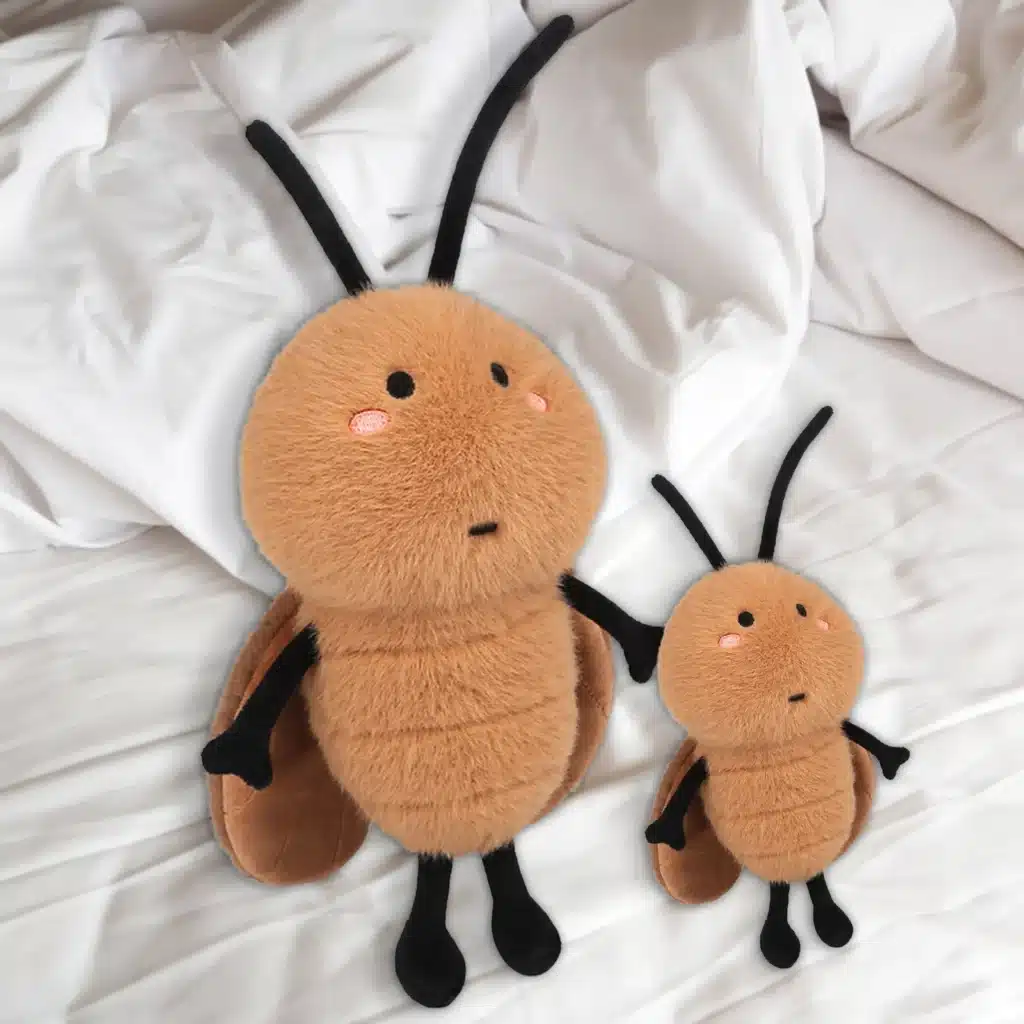 Two Plush Toy Cockroaches, One Large And One Small, With Soft Brown Bodies, Black Legs, And Antennae, Placed On A White Bedspread.