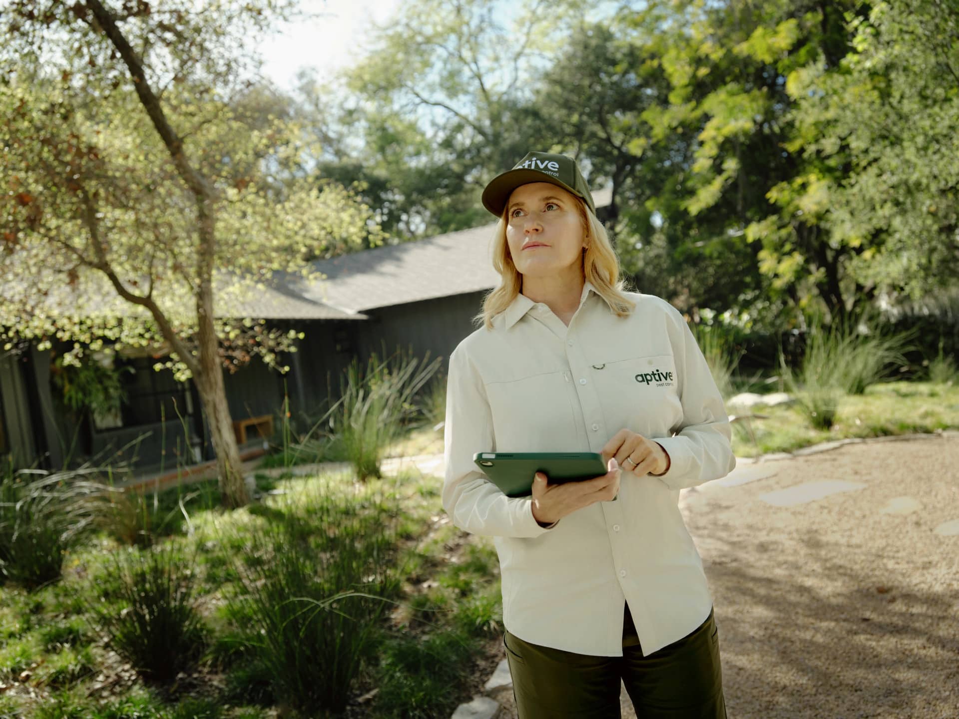 Aptive-Environmental-Female-Technician-Inspecting-Yard Female Aptive Environmental Technician Holding A Tablet And Inspecting The Surrounding Property In A Residential Yard.