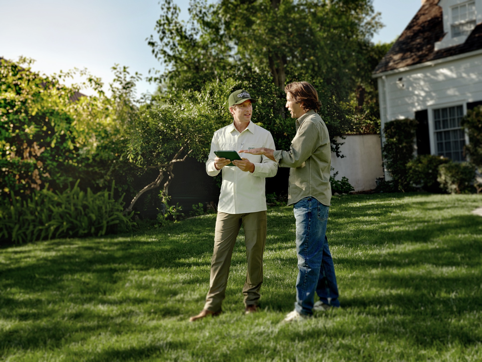 Aptive-Environmental-Technician-Consulting-Homeowner-Lawn Aptive Environmental Technician Holding A Tablet While Discussing Lawn Care Services With A Homeowner In A Residential Front Yard